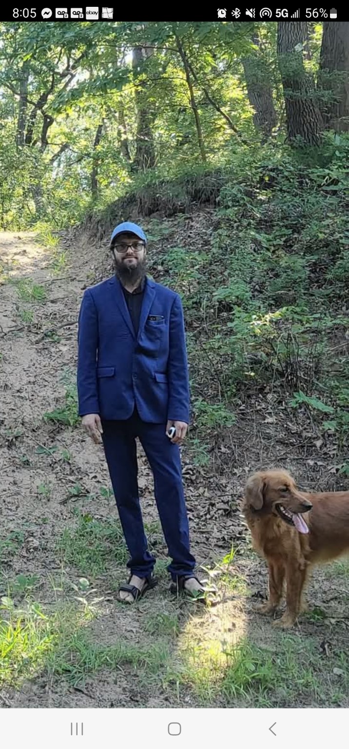 Abraham standing with his service dog Annie on a wooded path