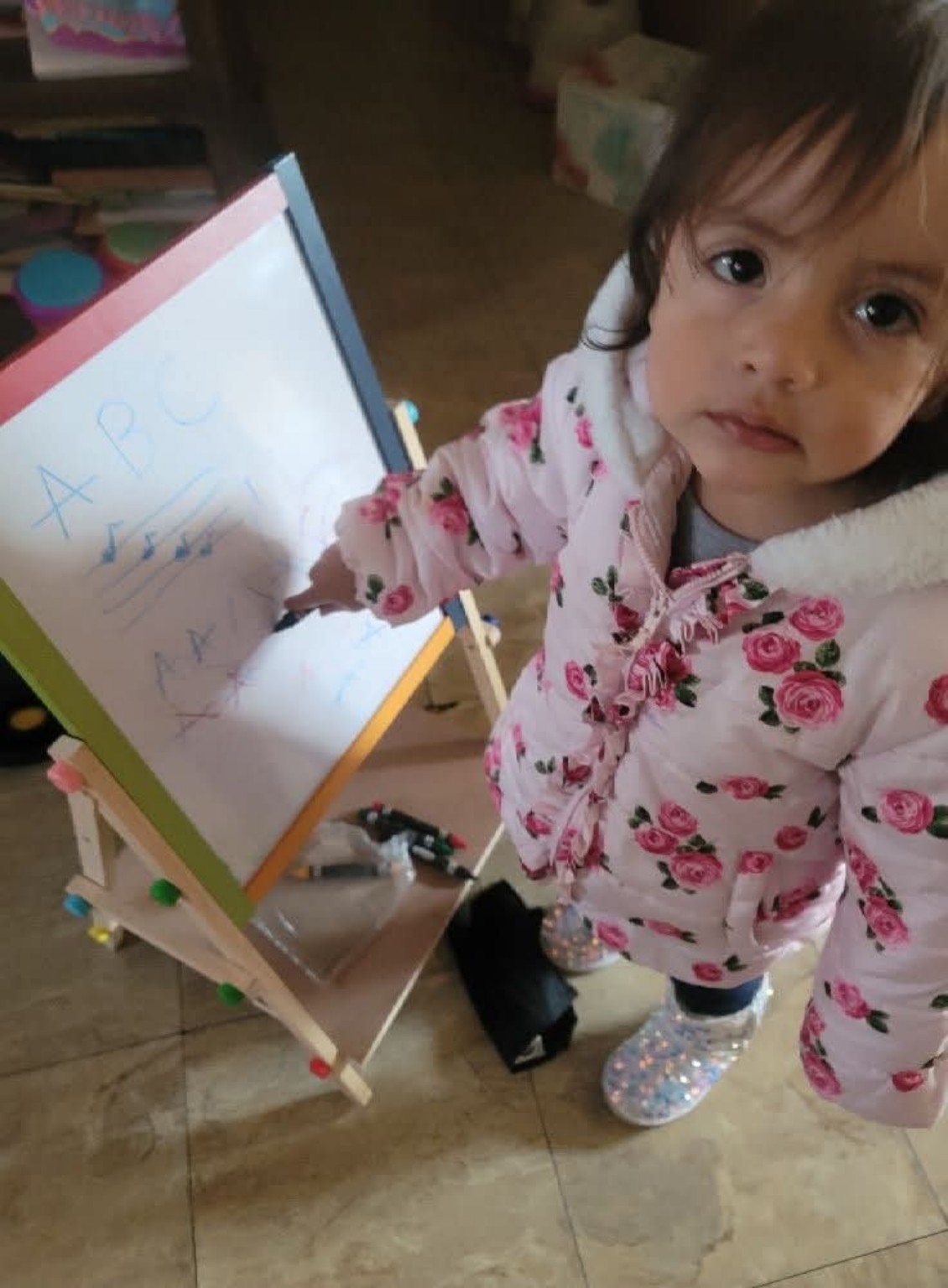 A young child standing beside an easel and practicing letters